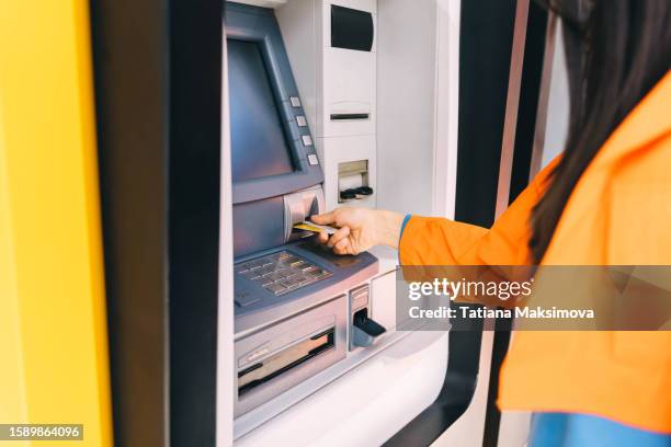 unrecognizable woman in bright cloth withdraws money from an atm. hand close-up. - paid absence stock pictures, royalty-free photos & images