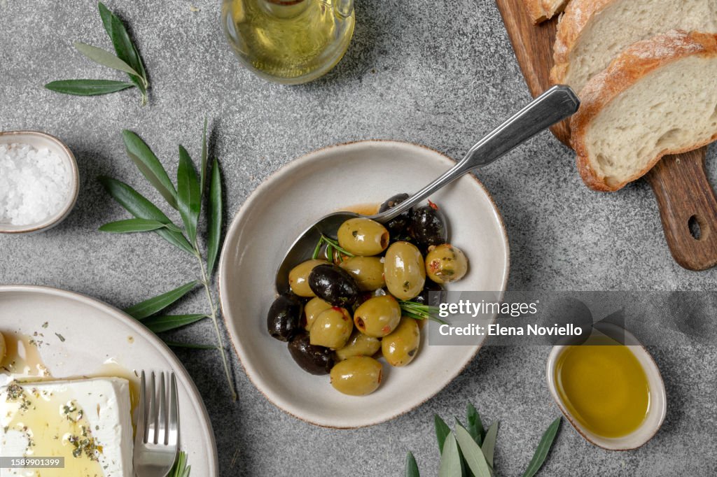 Different kinds of olives in olive oil with herbs with olive tree branches