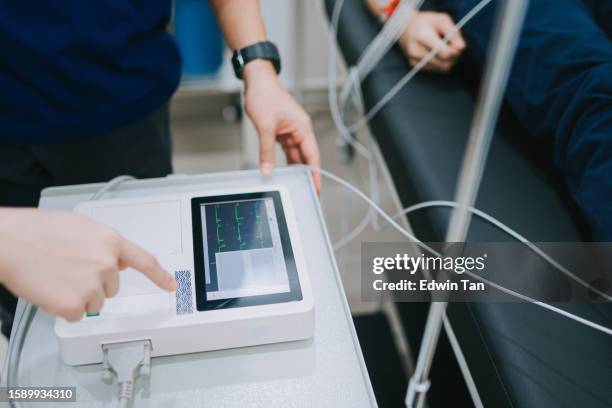 high angle asian chinese doctor nurse looking at ecg screen monitoring patient heart condition - hartritmestoornis stockfoto's en -beelden