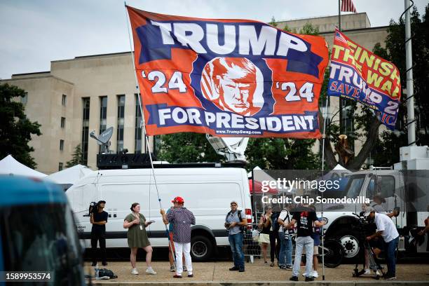 Supporter carries a large flag in support of Donald Trump television satellite trucks outside the E. Barrett Prettyman U.S. District Court House...
