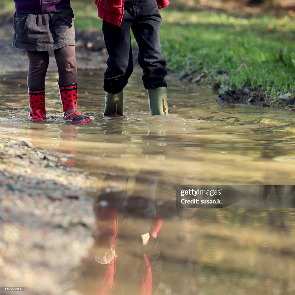 Holding hands while exploring muddy puddle.