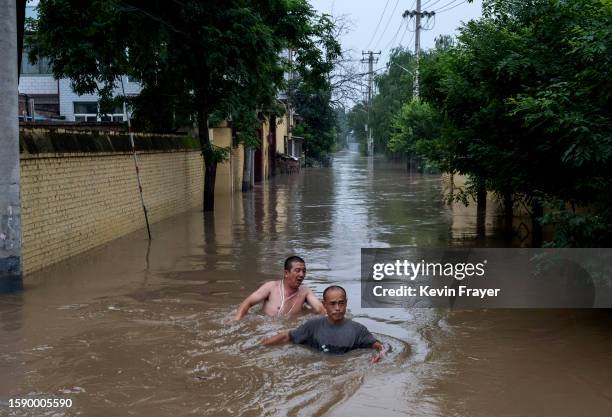 Local residents struggle in deep fast moving water as they make their way towards rescuers in a boat in an area inundated with floodwaters on August...