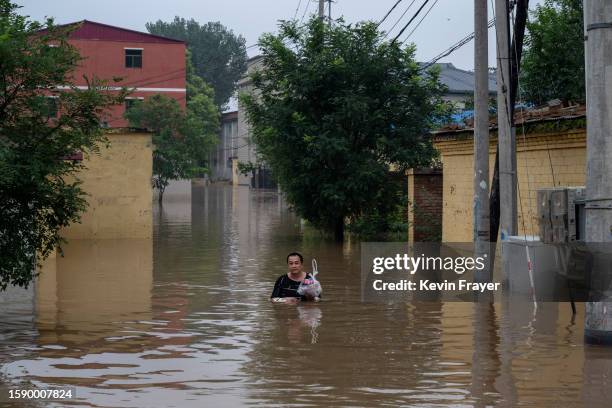 Local resident wades in chest deep floodwaters towards a rescue boat to be helped to safety in an area inundated with floodwaters on August 3, 2023...