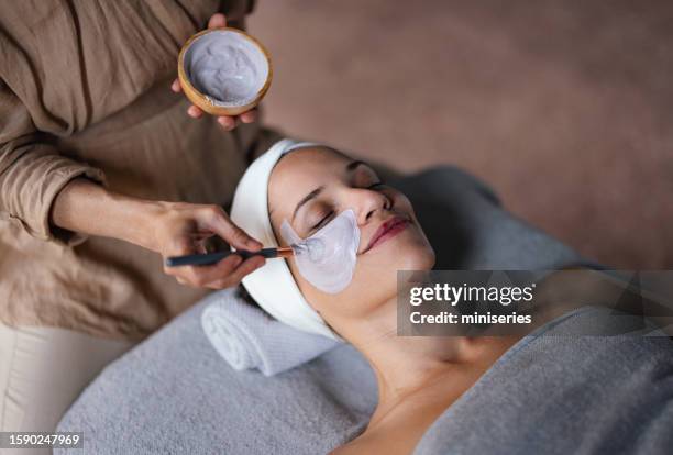 beautiful woman enjoying receiving a facial treatment at the spa - clay mask stock pictures, royalty-free photos & images