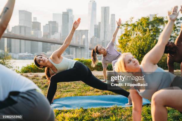 yoga class in the city at sunset with new york city skyline in the background - revolved triangle pose stock pictures, royalty-free photos & images