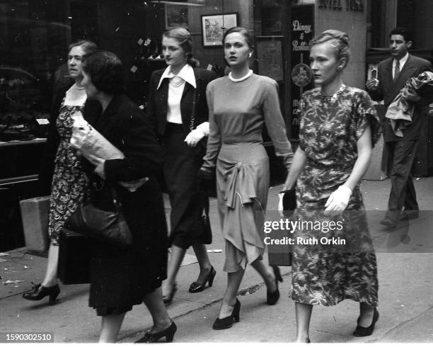 View of a group of women as they walk along a sidewalk, New York, New York, 1948. This photograph was originally part of a story about fashion...