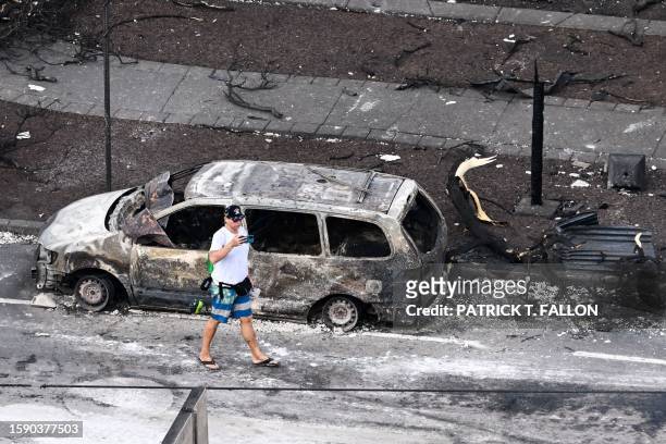 An aerial image taken on August 10, 2023 shows a person walking past a destroyed car in the aftermath of wildfires in western Maui in Lahaina,...