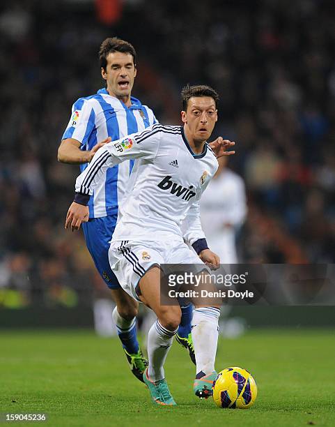 Mesut Ozil of Real Madrid CF passes the ball in front of Xavi Prieto of Real Sociedad de Futbol during the La Liga match between Real Madrid CF and...