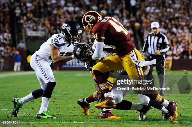 Russell Wilson of the Seattle Seahawks is tackled by Madieu Williams and DeAngelo Hall of the Washington Redskins during the NFC Wild Card Playoff...