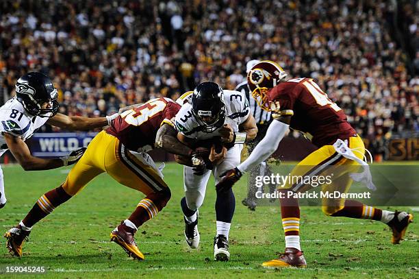 Russell Wilson of the Seattle Seahawks is tackled by Madieu Williams and DeAngelo Hall of the Washington Redskins during the NFC Wild Card Playoff...