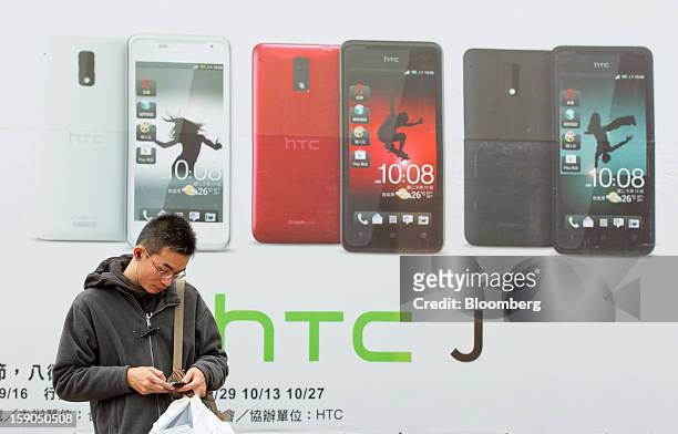 Man uses a mobile phone as he stands in front of an advertisement for HTC Corp.'s J smartphone in Taipei, Taiwan, on Sunday, Jan. 6, 2013. HTC is...