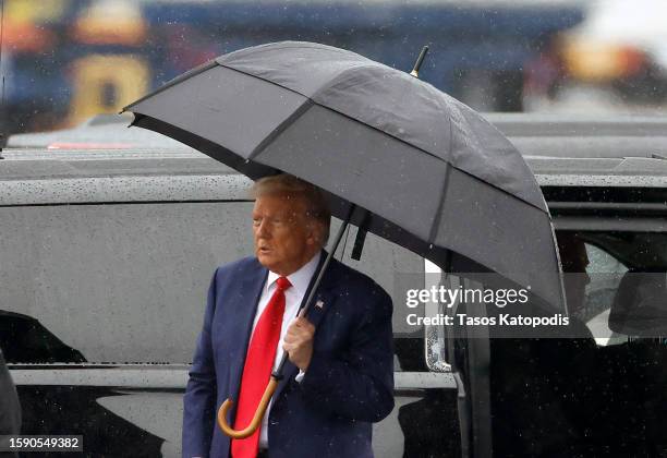 Former U.S. President Donald Trump holds an umbrella as he arrives at Reagan National Airport following an arraignment in a Washington, D.C. Court on...