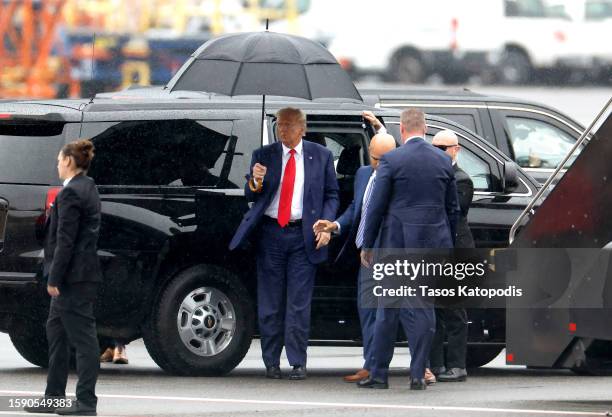 Former U.S. President Donald Trump holds an umbrella as he arrives at Reagan National Airport following an arraignment in a Washington, D.C. Court on...