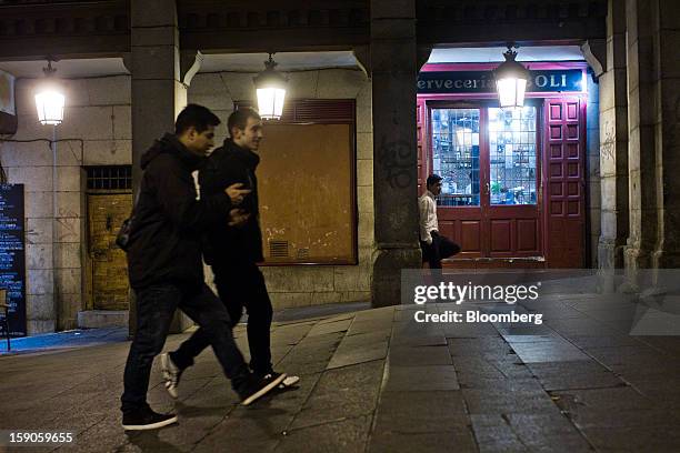 Pedestrians walk past a bar illuminated at night in Madrid, Spain, on Sunday, Jan. 6, 2013. In December, the Spanish parliament passed an energy law...