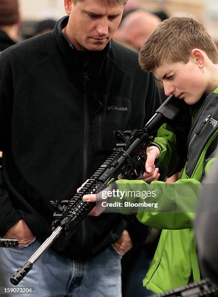 Boy holds a semi-automatic assault rifle for sale while his father watches at the Rocky Mountain Gun Show in Sandy, Utah, U.S., on Saturday, Jan. 5,...