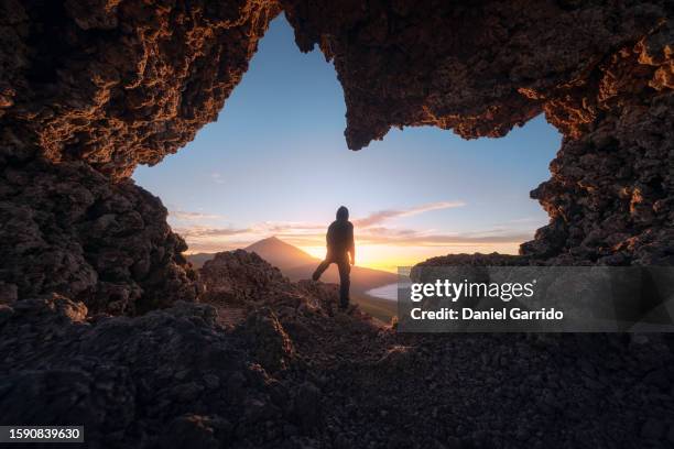 man silhouette gazing at teide from tenerife's stone arch, capturing the essence of teide from a tenerife stone arch at dusk - pico de teide stock-fotos und bilder