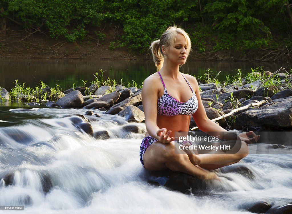 A woman meditating in the middle of a creek