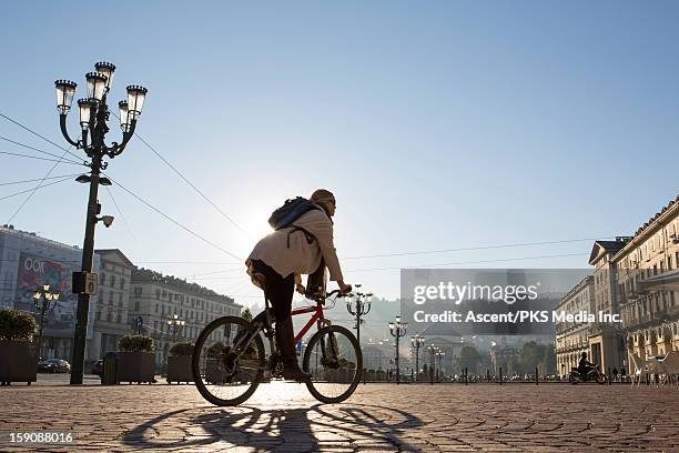 woman rides bicycle through urban piazza, sunrise - city bike foto e immagini stock