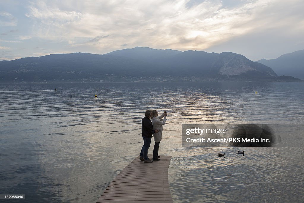 Couple stand on curving lake pier, take picture