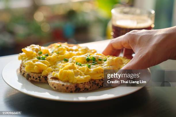 朝に健康的な朝食を楽しむときに、スクランブルエッグを上に乗せたトーストしたパンを持つ女性の手のトリミングされた画像 - パン　持つ　手　女性 ストックフォトと画像
