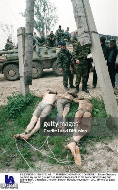 Three Chechen soldiers lay on the ground as Russian troops look at them after undressing and killing them, Dagestan-Chechen border, Russia, November...
