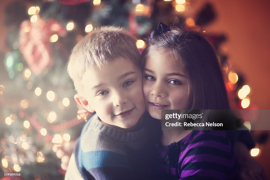 Children embracing in front of Christmas tree