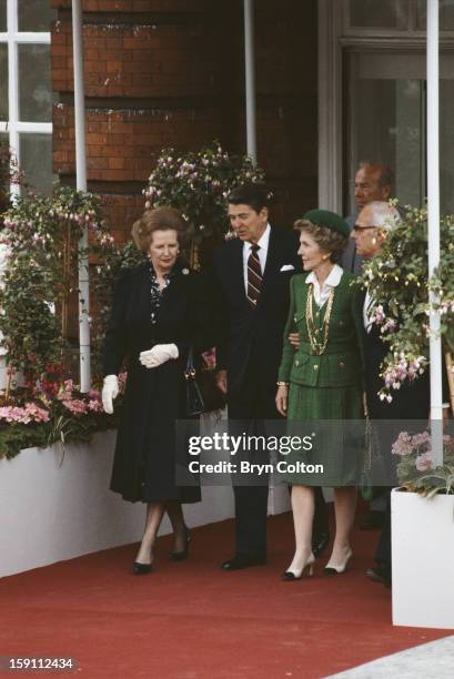 British Prime Minister Margaret Thatcher and her husband Denis Thatcher walk with US President Ronald Reagan and his wife Nancy Reagan, as they...
