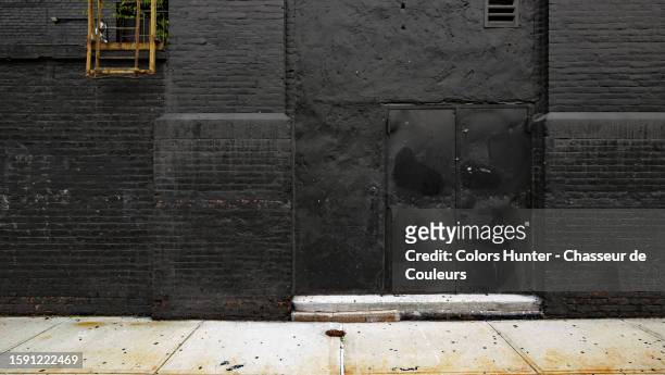 black painted brick wall with door, yellow fire ladder and concrete sidewalk in manhattan, new york state, united states - hunter, new york stock-fotos und bilder