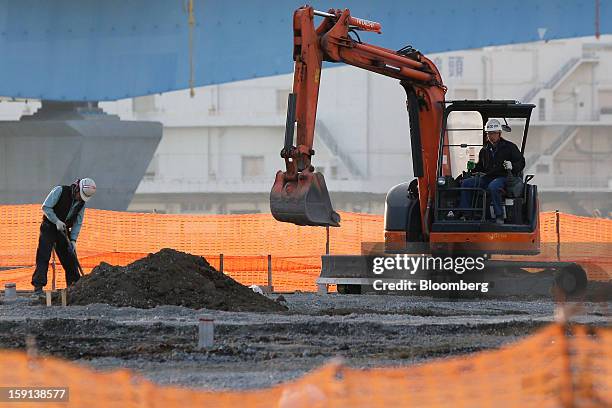 Hitachi Construction Machinery Co. Excavator, right, operates as a worker labors on a construction site in Tokyo, Japan, on Tuesday, Jan. 8, 2013....