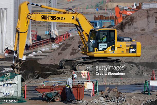 Worker, front, labors while an excavator operates on a construction site in Tokyo, Japan, on Tuesday, Jan. 8, 2013. Prime Minister Shinzo Abe aims to...
