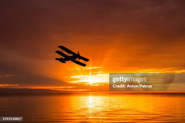 vintage biplane silhouette at sunset over the sea - biplane stock pictures, royalty-free photos & images