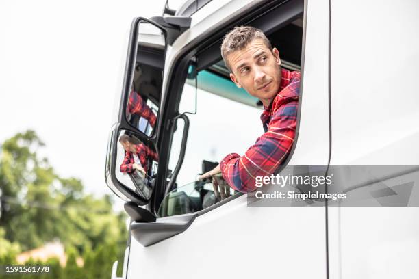 driver of a semi truck looks backwards from the open window of his cab as he reverses the truck to a loading point. - reversing stock pictures, royalty-free photos & images