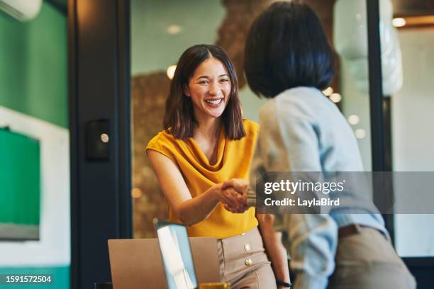 fröhliche geschäftsfrauen, die sich im besprechungsraum die hände schütteln - handshake stock-fotos und bilder