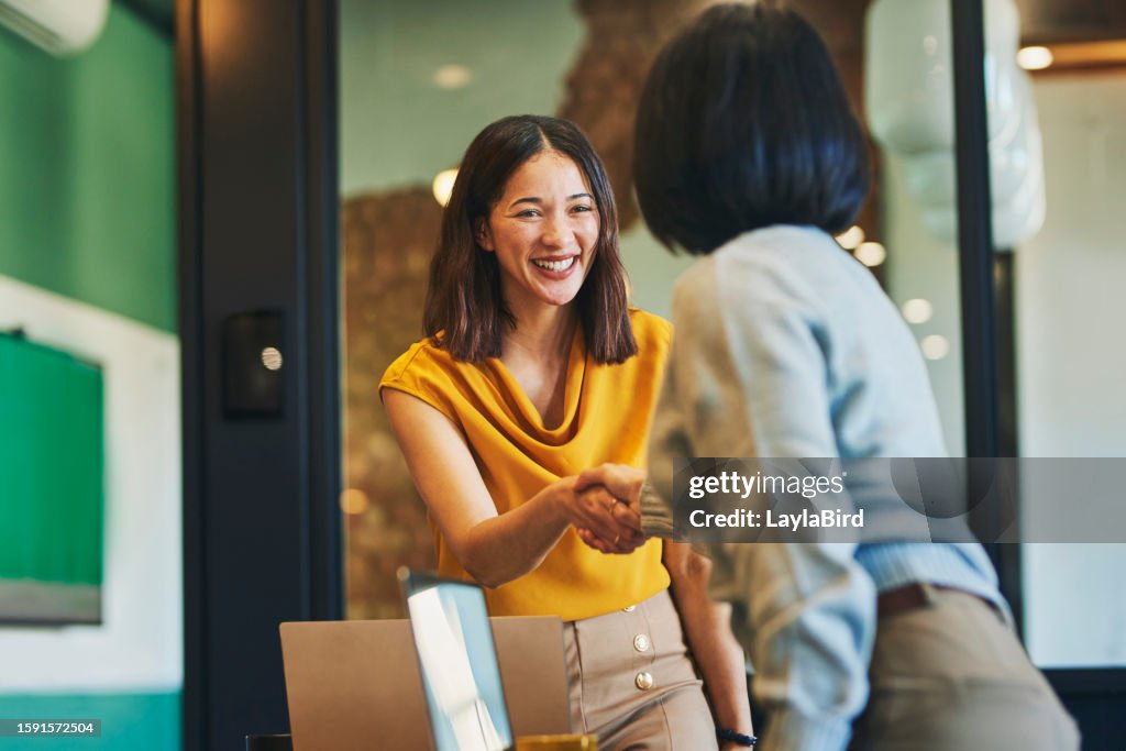 Donne d'affari allegre che stringono la mano nella sala riunioni