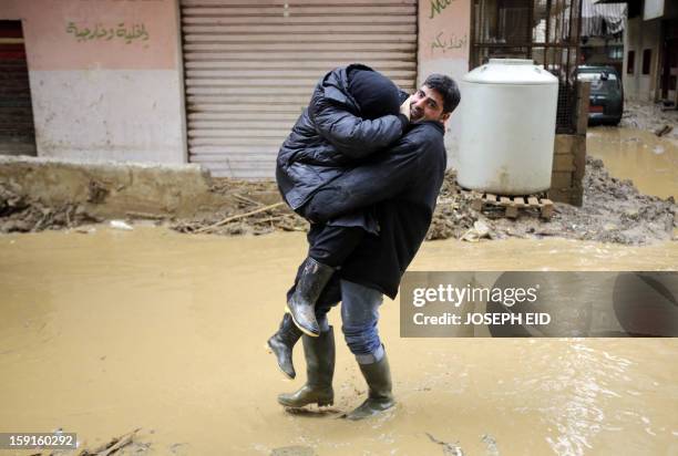 Man carries a woman through a flooded alley in Beirut's southern suburb of Hayy al-Sellum on January 9, 2013 as heavy rains and high speed winds hit...