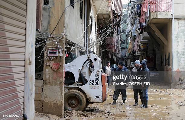 Lebanese men watch on as a bulldozer works on removing garbage, mud and water from the flooded streets in Beirut's southern suburb of Hayy al-Sellum...