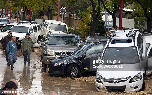 Israelis walk past damaged cars in Beit Hefer near the Meditrranean coastal city of Netanya, north of Tel Aviv, on January 9 after heavy rains...