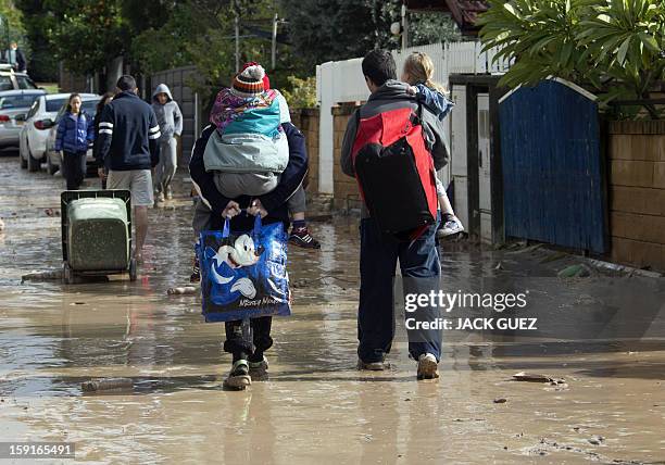 Israelis carry their children as they walk through muddy streets due to heavy rains overnight that caused flooding in Beit Hefer, near the...