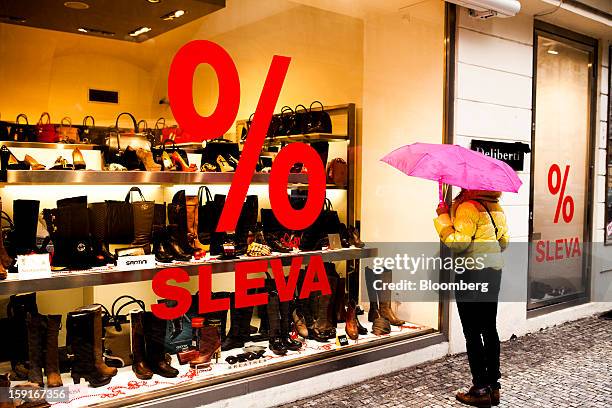 Pedestrian holds an umbrella as she looks in the window of a shoe store offering sale prices in Prague, Czech Republic, on Tuesday, Jan. 8, 2013. The...