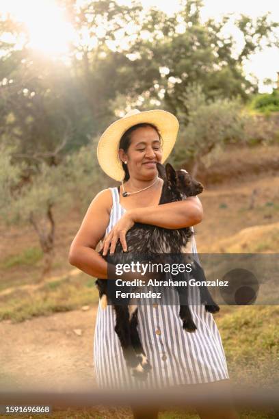 latin woman holding a little goat in a rural area - geitje stockfoto's en -beelden