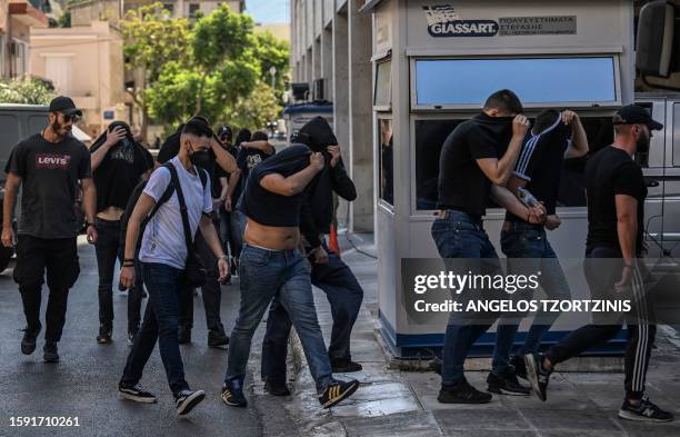 Football fans, most of them from Croatia, cover their faces while leaving the Athens Police Headquarters in Athens, on August 11 as they are being...
