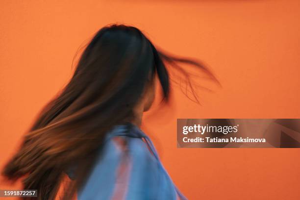 rear view unrecognizable woman with flying hair on orange background. defocused, blurred motion. - schwindelig stock-fotos und bilder