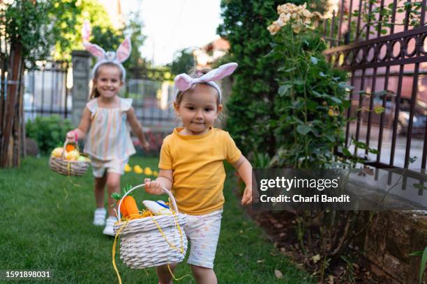 イースターエッグでいっぱいのイースターバスケットを持って走る幼児の女の子 - easter bunny ears ストックフォトと画像