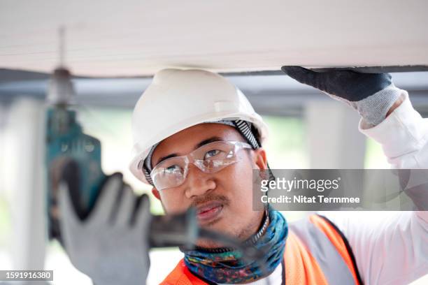 built quality control and safety culture during the construction project. shot of a construction worker using a cordless power screwdriver to attach a ceiling wall and working in a safe condition in a house construction. - technician stock pictures, royalty-free photos & images