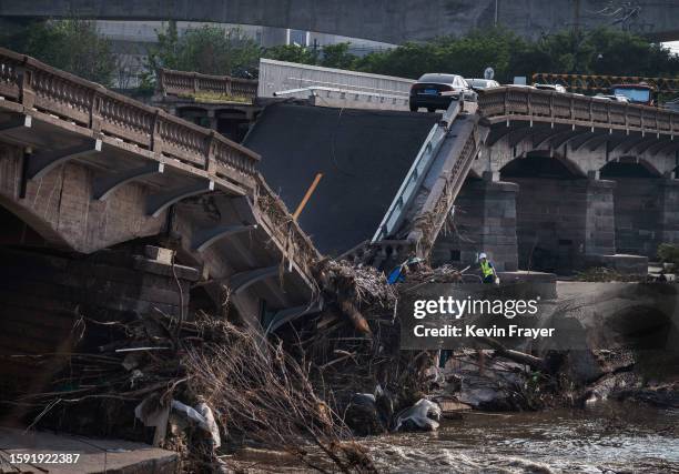 Abandoned cars are seen as a worker inspects a bridge that collapsed in recent days after a flash flood caused by heavy rainfall on August 4, 2023 in...