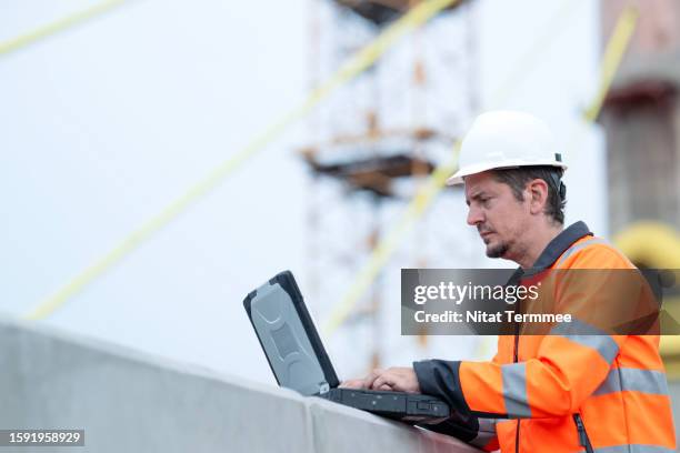 real-time communication and collaboration with construction management solution. shot of a male construction project manager on field operation while using a laptop computer to follow up project task with his team at bridge construction site. - bim stock pictures, royalty-free photos & images