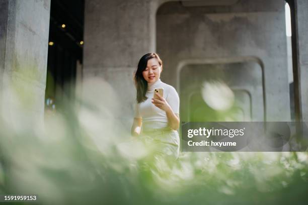 asian woman using smartphone in a modern office park - kantoorpark stockfoto's en -beelden