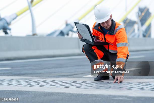 using bim technology in the construction industry to ensuring compliance with environmental requirements. a male civil engineer in field operation holding a laptop to inspect the drainage and speed up the water flow of a water drain in a suspension bridge - quality sport images 個照片及圖片檔