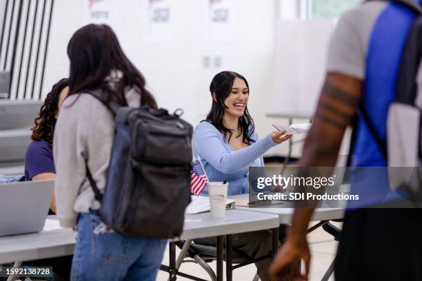 cheerful female election worker hands ballot to unseen voter - voter registration stock pictures, royalty-free photos & images