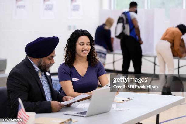 diverse poll volunteers discuss ballot while people vote in background - political party stock pictures, royalty-free photos & images